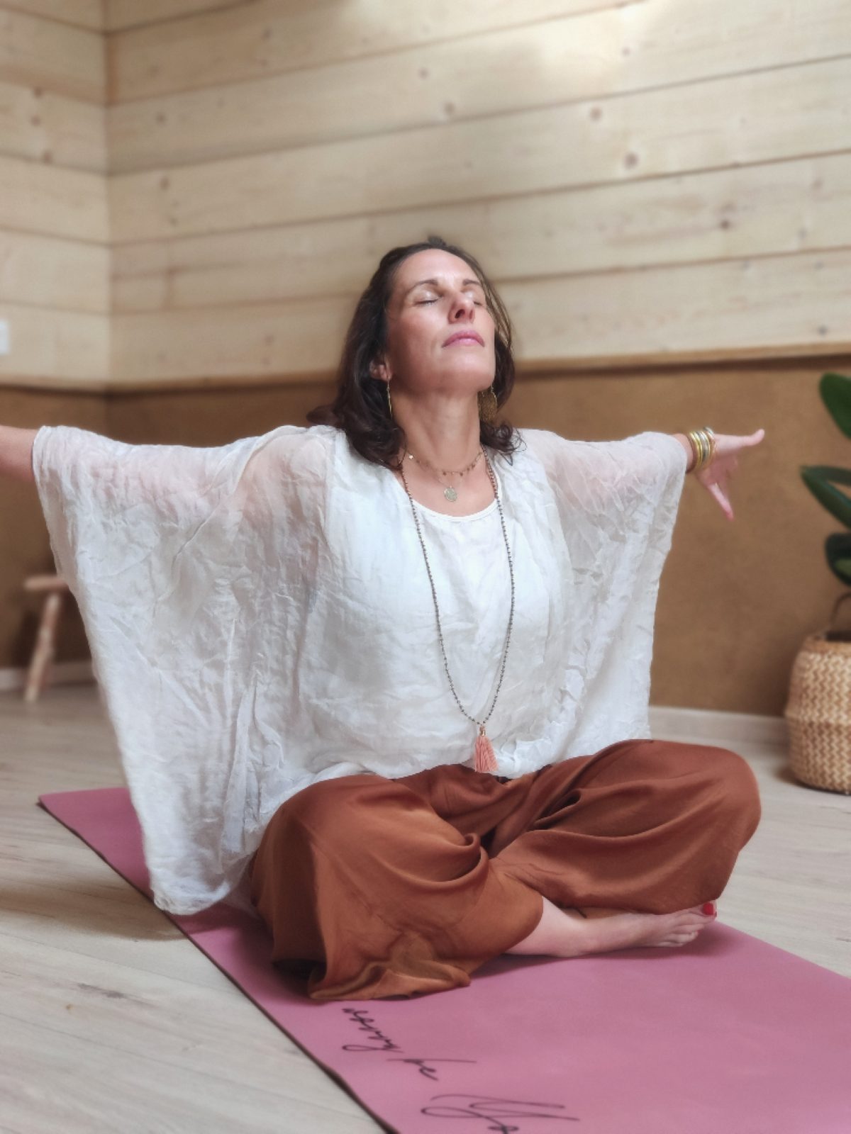 Angélique en méditation, bras ouverts, dans son studio à Dax