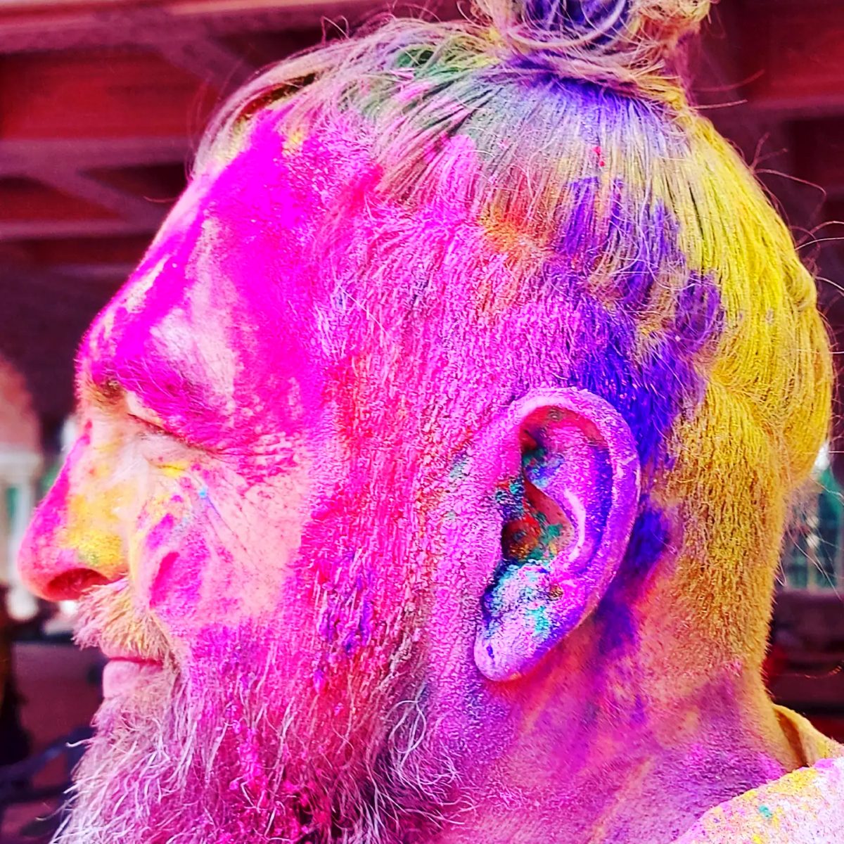 Visage de profil entièrement recouvert de poudres roses, jaunes et violettes pendant Holi