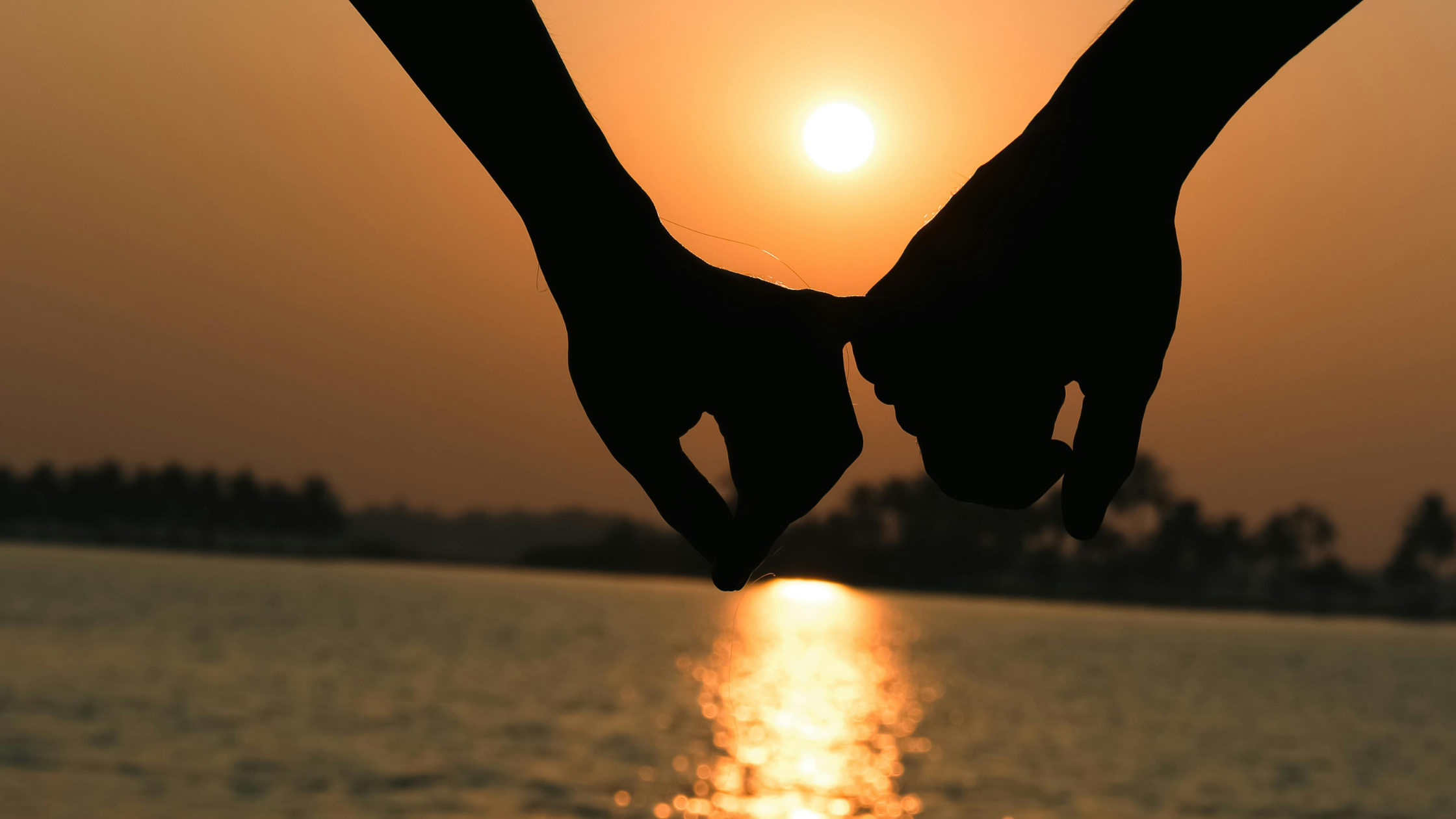 Deux mains qui se lâchent doucement, en silhouette devant un coucher de soleil sur l'eau