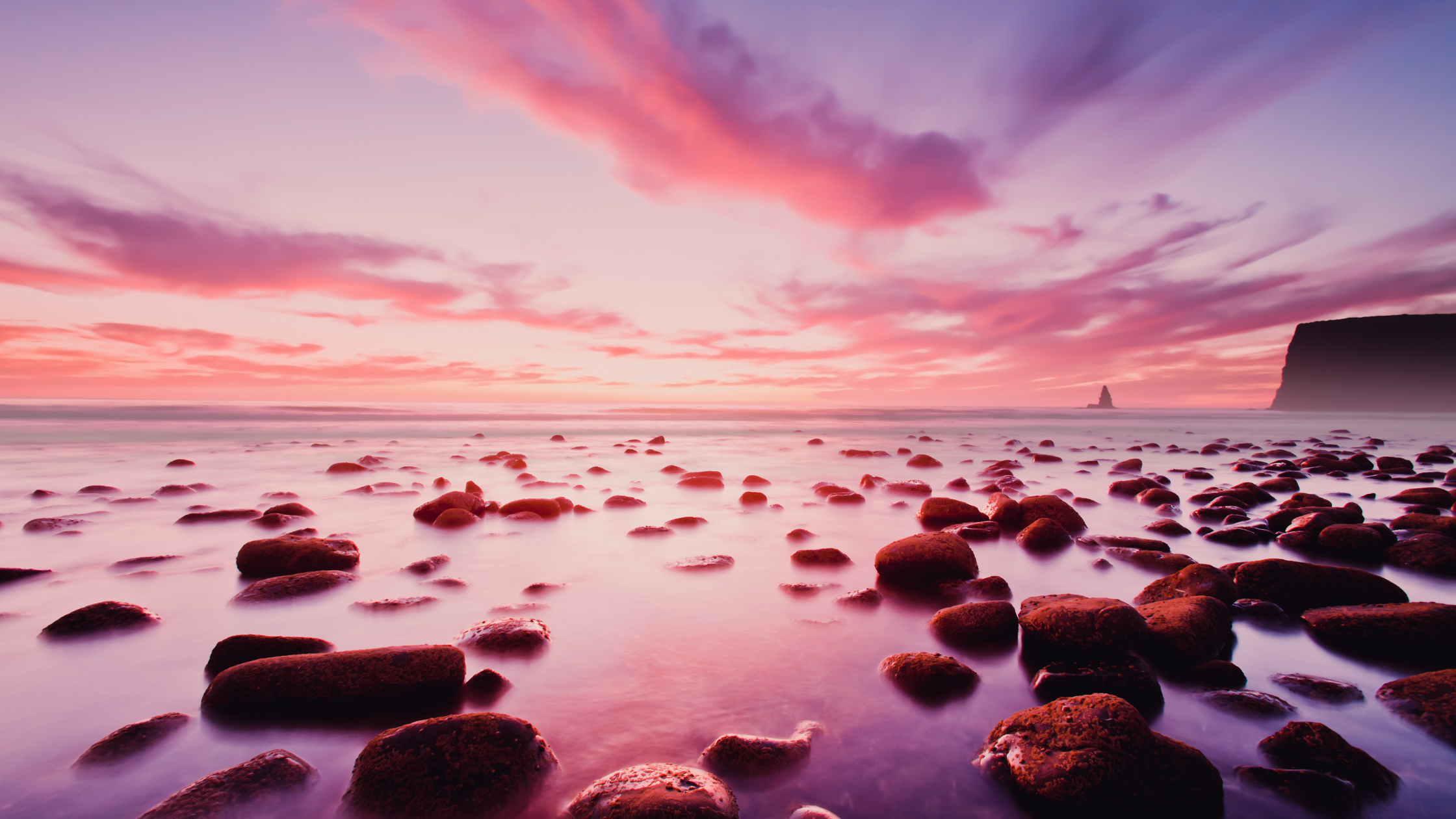 Plage de galets au coucher du soleil, ciel rose et mauve