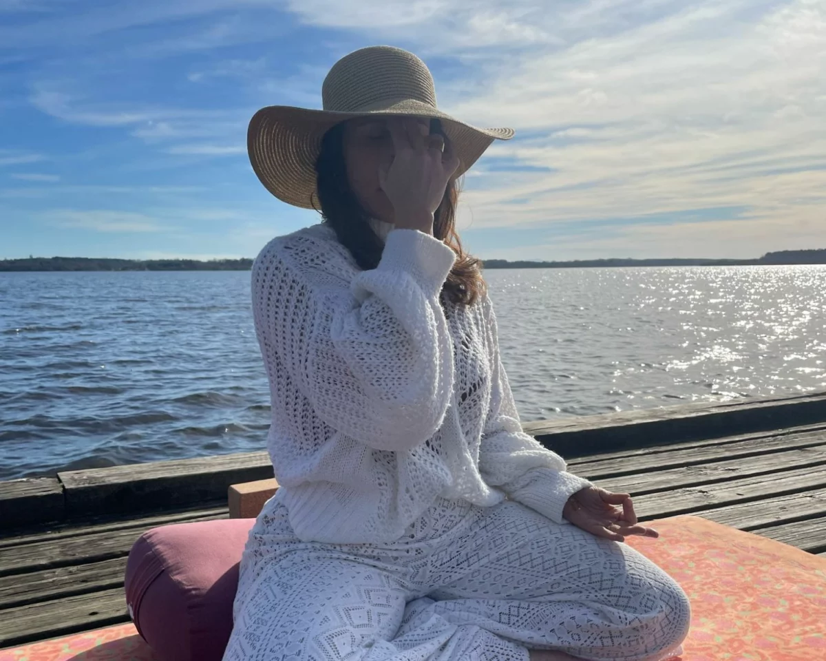Angélique pratique la respiration alternée, assise sur son tapis au bord d'un lac landais